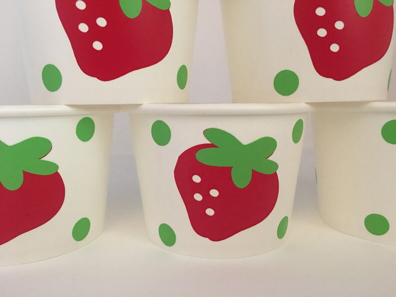 May include: Set of six white paper cups with a red strawberry and green leaves design. The cups have green polka dots.