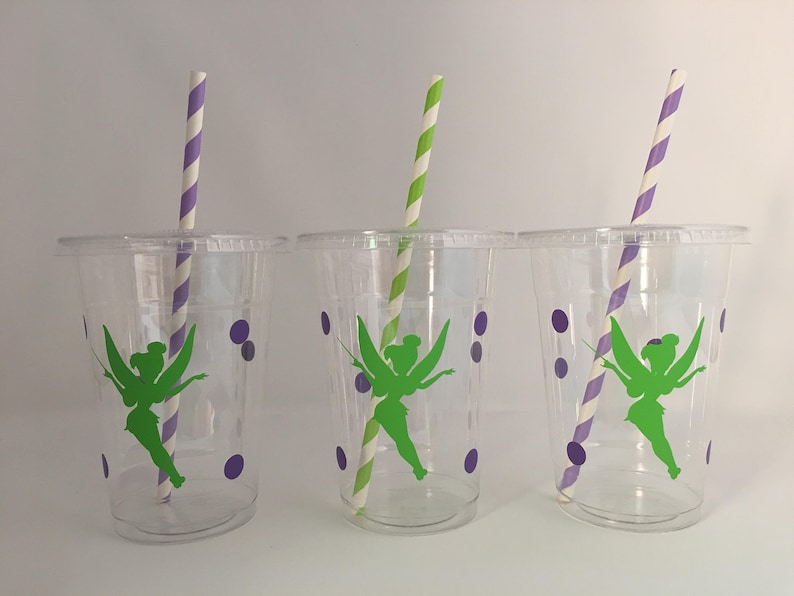 May include: Three clear plastic cups with purple polka dots and a green fairy silhouette design. Each cup has a purple and white striped straw.