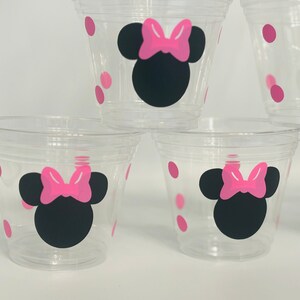 Puede incluir: Cuatro vasos de pl&aacute;stico transparentes con lunares rosas y un dise&ntilde;o de Minnie Mouse negro y rosa.