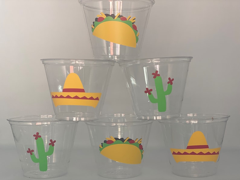 May include: Six clear plastic cups with colorful designs. The designs include a yellow sombrero, a green cactus with red flowers, and a yellow taco.