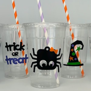 May include: Five clear plastic cups with straws and Halloween-themed designs. The designs include a ghost, a spider, a witch's hat, a pumpkin, and the words "trick or treat".