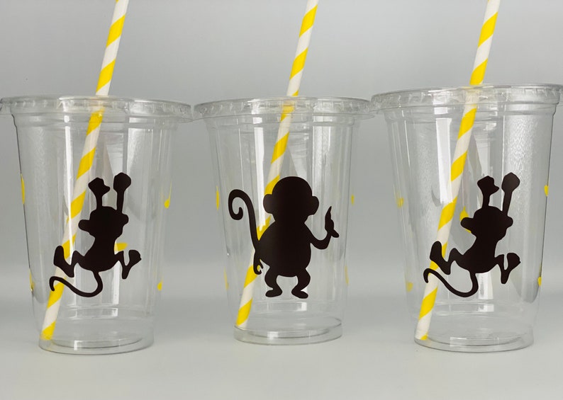 May include: Three clear plastic cups with yellow striped straws. Each cup has a black silhouette of a monkey on it.
