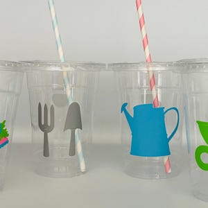 Pu&ograve; includere: Quattro bicchieri di plastica trasparente con cannucce di carta colorate e adesivi a tema giardinaggio. Gli adesivi includono un cappello, una forchetta e una vanga, un annaffiatoio e un carretto.