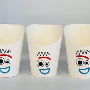 May include: Three white paper containers with a cartoon face design. Each container has a black squiggly hair design, a red eyebrow, two black eyes, and a blue smiling mouth. The containers are open at the top and are likely for holding food items.