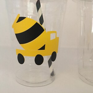 May include: Two clear plastic cups with yellow and black construction truck designs. The cups are decorated with a cement mixer truck and a dump truck.