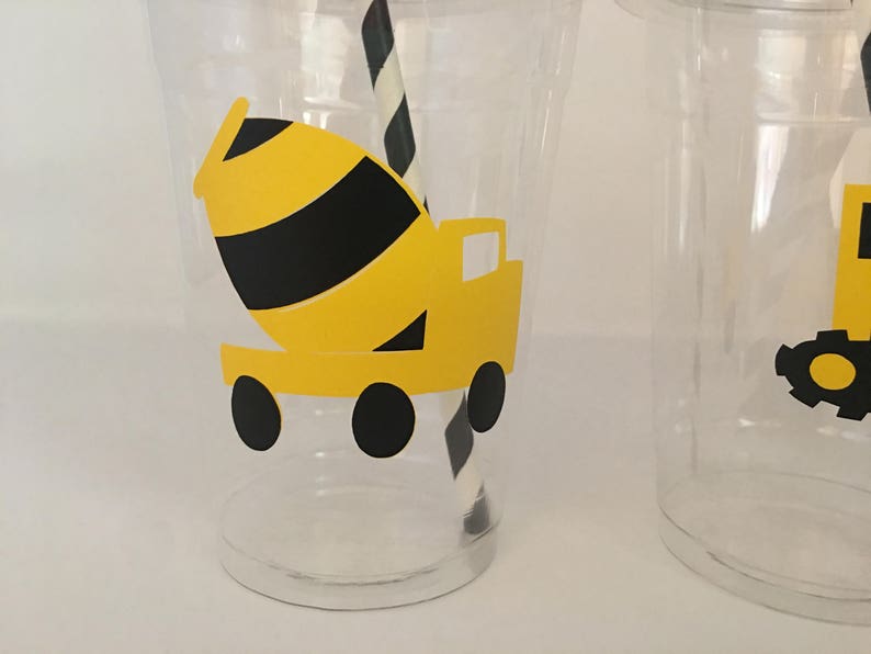 May include: Two clear plastic cups with yellow and black construction truck designs. The cups are decorated with a cement mixer truck and a dump truck.