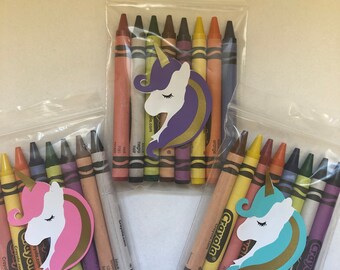 Op de afbeelding: Drie doorzichtige zakken met elk een set Crayola-kleurpotloden. Elke zak heeft een eenhoofd in een andere kleur. De kleurpotloden zijn in verschillende kleuren, waaronder rood, oranje, geel en paars.