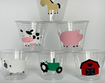 May include: Six clear plastic cups with farm animal designs. The cups feature a horse, cow, pig, tractor, and barn.
