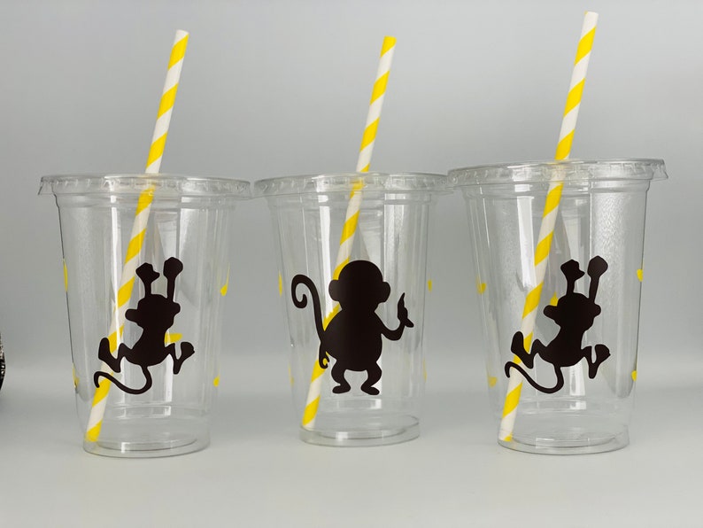 May include: Three clear plastic cups with black monkey silhouettes and yellow and white striped straws.