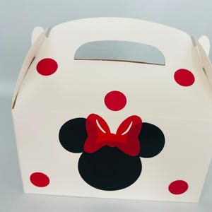 Puede incluir: Caja de regalo blanca con un dise&ntilde;o de Minnie Mouse rojo y negro. La caja tiene un asa y lunares rojos.