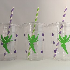 May include: Three clear plastic cups with green fairy silhouettes and purple polka dots. Each cup has a striped straw.