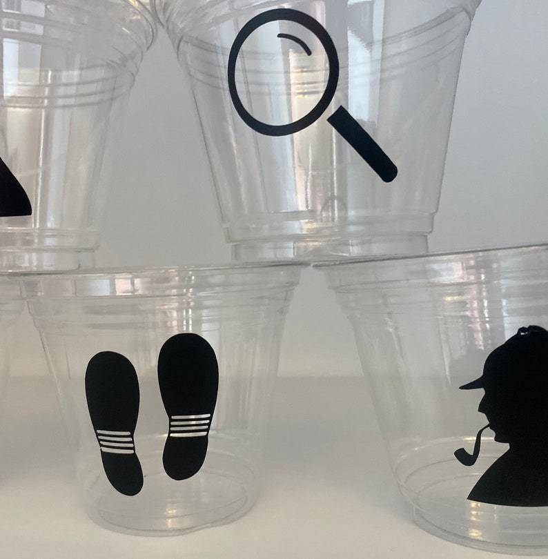 以下が含まれることがあります： 黒いシルエットのデザインが施された透明なプラスチックカップ4つ。デザインには、虫眼鏡、足跡2つ、パイプを持った探偵が含まれています。