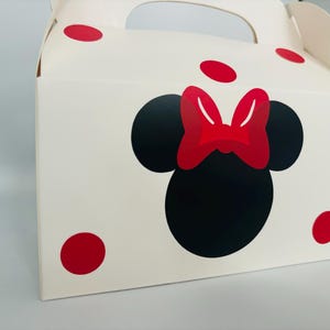 Puede incluir: Caja de cart&oacute;n blanca con un dise&ntilde;o de Minnie Mouse rojo y negro. La caja tiene un asa y lunares rojos.