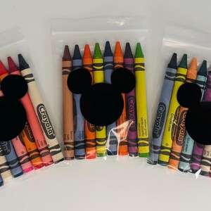 May include: Three clear plastic bags each containing a set of colorful crayons. Each bag has a black Mickey Mouse head sticker. The crayons are various colors, including yellow, blue, red, and orange. The brand name "Crayola" is visible on the crayons.