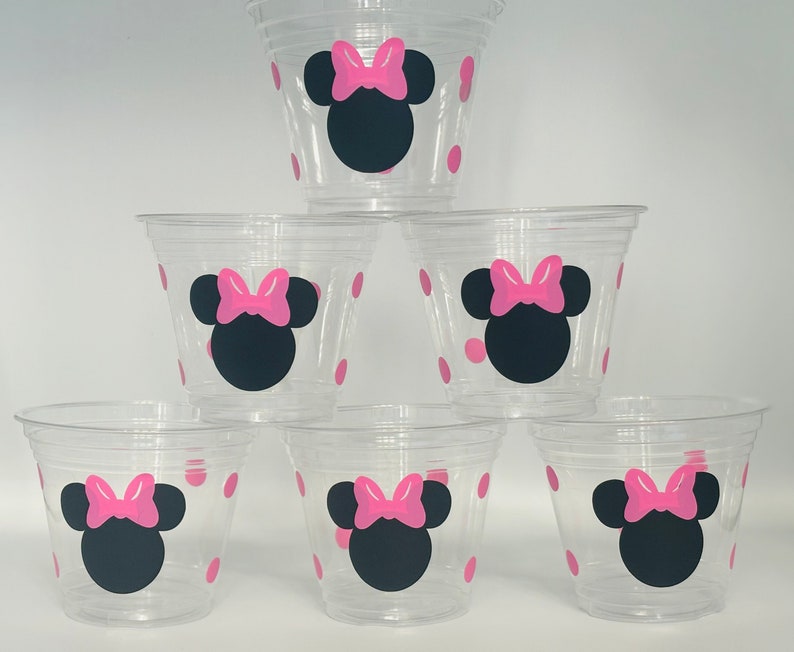 Puede incluir: Seis vasos de pl&aacute;stico transparentes con lunares rosas y un dise&ntilde;o de Minnie Mouse negro y rosa.