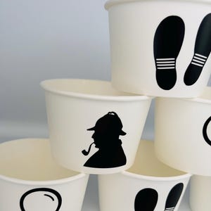Puede incluir: Conjunto de seis vasos de papel blanco con dise&ntilde;os de silueta negra. Los dise&ntilde;os incluyen una lupa, un detective con una pipa y huellas.