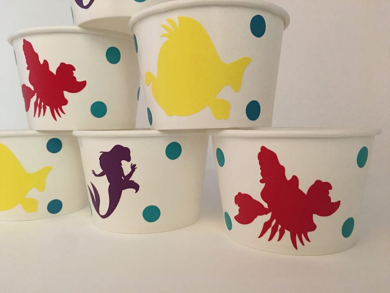 May include: Set of six white paper cups with colourful cartoon characters. The cups feature a mermaid, a yellow fish, and a red lobster. The cups are decorated with teal polka dots.