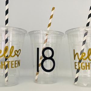 May include: Three clear plastic cups with black and white striped straws. The cups have gold lettering that says "hello eighteen" and "18".