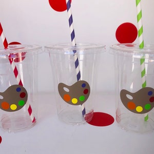 May include: Three clear plastic cups with colorful striped straws and a paint palette sticker on each cup. The cups are perfect for a party or event.