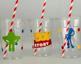 Puede incluir: Tres vasos de plástico transparentes con pajitas de rayas rojas y blancas. Cada vaso tiene un diseño de personaje de Toy Story diferente: un extraterrestre verde, las palabras "Toy Story" con un "Toy" amarillo y un "Story" rojo, y un Woody azul. Cada vaso tiene lunares rojos, azules y amarillos.