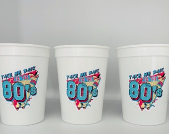 May include: Three white plastic cups with a retro 80s design. The cups have a blue, pink, and black graphic with the text "Take Me Back to the 80's".