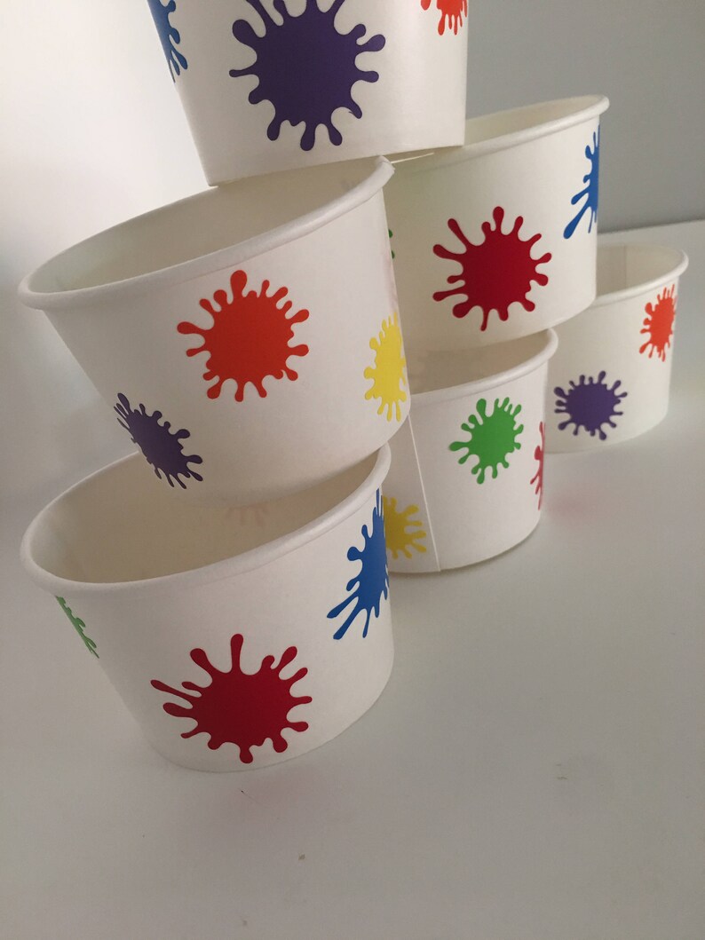 K&ouml;nnte beinhalten: Ein Stapel aus sechs wei&szlig;en Pappbechern mit bunten Farbklecksen. Die Becher sind pyramidenf&ouml;rmig gestapelt, wobei der gr&ouml;&szlig;te Becher unten und der kleinste oben liegt. Die Farbkleckse sind in verschiedenen Farben, darunter Rot, Orange, Gelb, Gr&uuml;n, Blau und Lila.