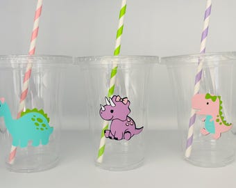 May include: Three clear plastic cups with straws and dinosaur stickers. The cups have pink, purple, and green dinosaurs with pink, green, and blue accents. The straws are pink and white, green and white, and purple and white.