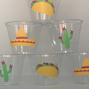 May include: Six clear plastic cups with different Mexican-themed designs. The designs include a sombrero, a cactus, and a taco.