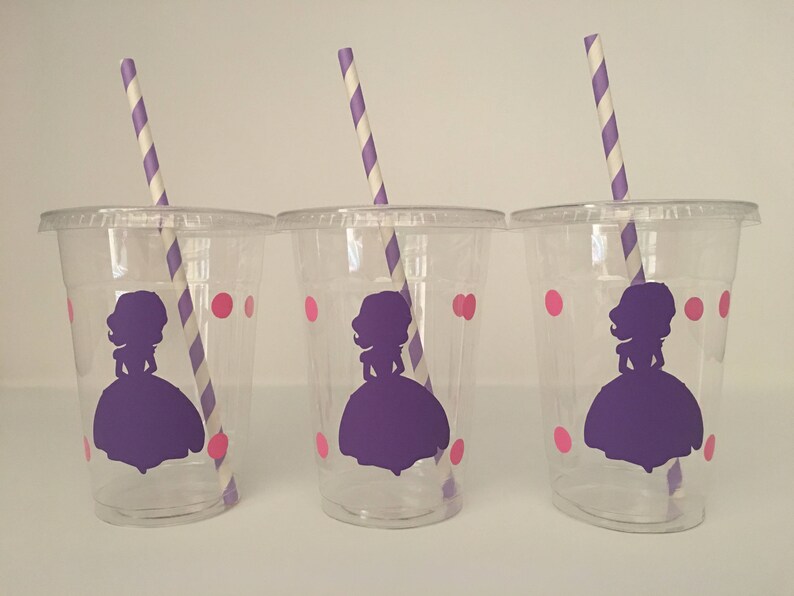 May include: Three clear plastic cups with purple and pink designs. Each cup has a purple silhouette of a princess with a crown and a pink polka dot pattern. Each cup has a striped straw.