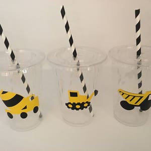May include: Three clear plastic cups with black and white striped straws. Each cup has a yellow and black construction vehicle sticker on the front. The vehicles are a cement mixer, a backhoe, and a dump truck.