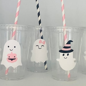 May include: Five clear plastic cups with pink and black striped straws. Each cup has a ghost sticker with different designs, including a pumpkin, a bow, a witch's hat, and a bow tie.