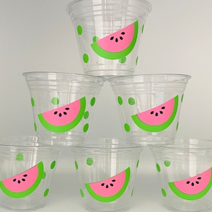 May include: Six clear plastic cups with watermelon designs. Each cup has a green watermelon slice with pink flesh and black seeds on a white background with green polka dots.