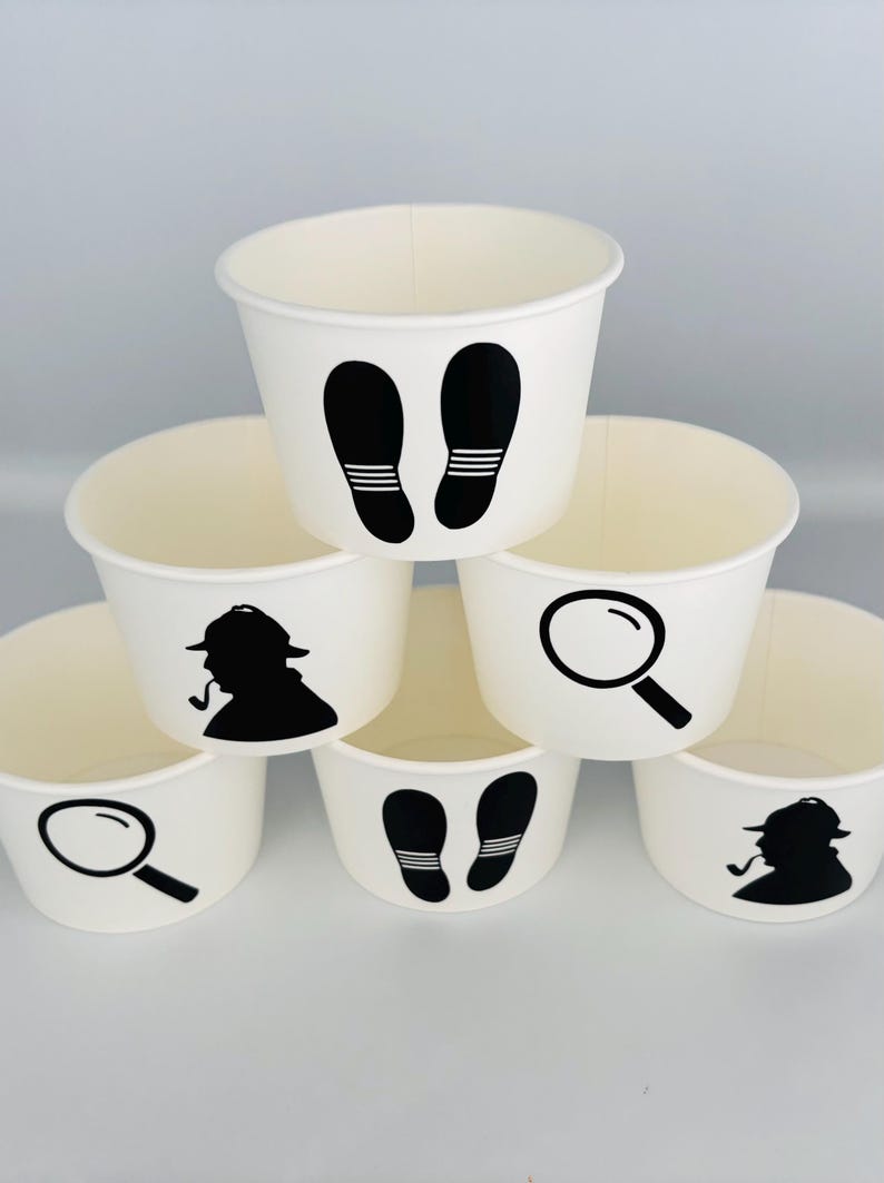 Puede incluir: Seis vasos de papel blancos con siluetas negras de una lupa, huellas y un detective. Los vasos est&aacute;n apilados en forma de pir&aacute;mide.