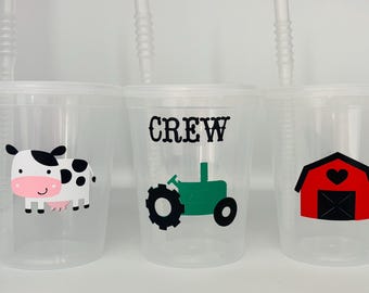 May include: Three clear plastic cups with straws. The cups have different farm-themed designs: a cow, a tractor, and a barn. The cup with the tractor has the word "CREW" printed on it.