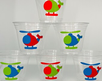 May include: Six clear plastic cups with red, blue, and green helicopter designs. The helicopters have red, blue, and green bodies with white blades.