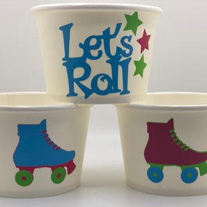 May include: Three white paper cups with different designs. The top cup has the text "Let's Roll" in blue with green and red stars. The middle cup has a blue roller skate with green wheels. The bottom cup has a maroon roller skate with green wheels.