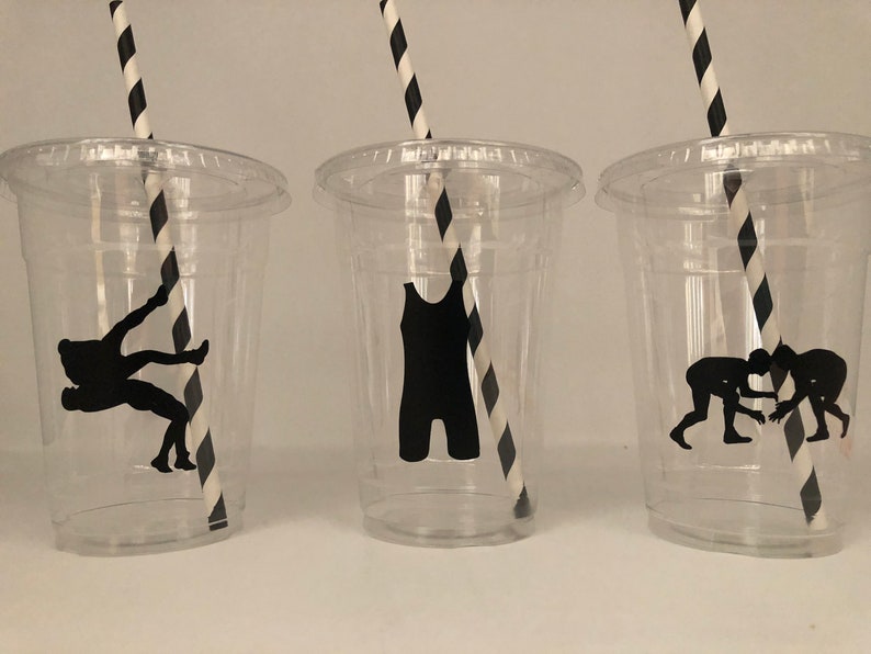 K&ouml;nnte beinhalten: Drei durchsichtige Plastikbecher mit schwarz-wei&szlig; gestreiften Strohhalmen. Jeder Becher hat eine schwarze Silhouette einer anderen Wrestling-Pose.