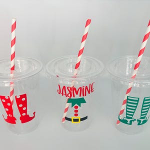 May include: Three clear plastic cups with red and white striped straws. Each cup has a different elf design with the name "Jasmine" on one cup.