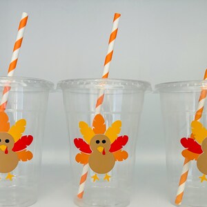 May include: Three clear plastic cups with orange and white striped straws. Each cup has a Thanksgiving turkey sticker with orange, yellow, and red feathers.