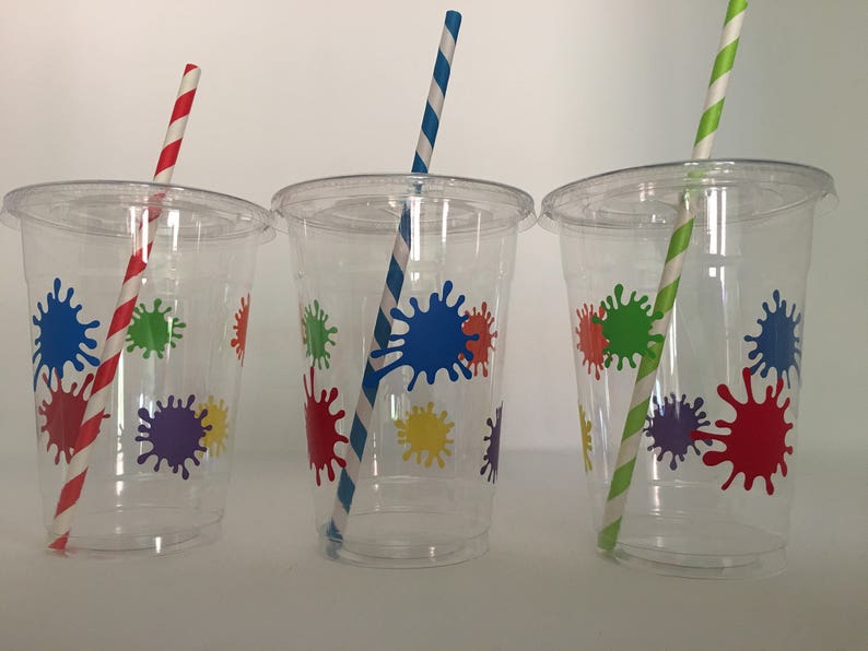 May include: Three clear plastic cups with colorful paint splatter designs and matching striped straws. The straws are red, blue, and green.