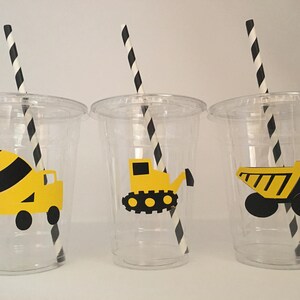 May include: Three clear plastic cups with black and white striped straws. Each cup has a yellow construction vehicle sticker on the front. The vehicles are a cement mixer, a bulldozer, and a dump truck.