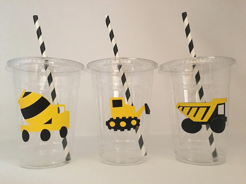 May include: Three clear plastic cups with black and white striped straws. Each cup has a yellow construction vehicle sticker on the front. The vehicles are a cement mixer, a bulldozer, and a dump truck.