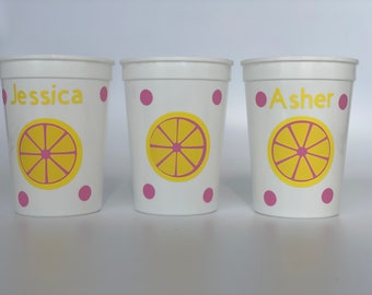 May include: Three white plastic cups with pink polka dots and a yellow lemon slice design. The cups are personalized with the names "Jessica", "Asher", and a blank cup.