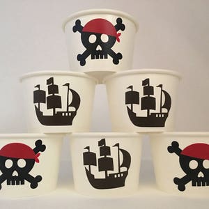 Peut inclure: Six gobelets en papier blanc avec des motifs pirates noirs et rouges. Les motifs comprennent un cr&acirc;ne et des os crois&eacute;s, un navire pirate et un chapeau de pirate.