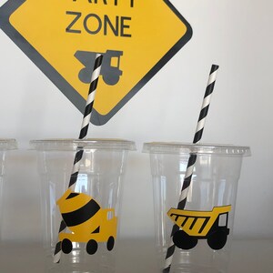 May include: Clear plastic cups with black and white striped straws. Each cup has a yellow construction vehicle sticker. The sign above reads "Party Zone" with a yellow construction truck graphic.