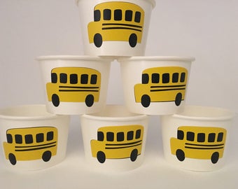 Op de afbeelding: Zes gele papieren bekers met een zwart en geel schoolbusontwerp. De bekers zijn in een piramidevorm gestapeld.