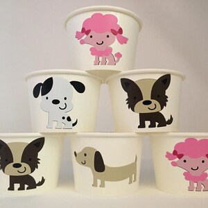 Pu&ograve; includere: Sei bicchieri di carta bianchi con diversi disegni di animali. I bicchieri presentano un barboncino rosa, un cane bianco e nero, un cane marrone, un bassotto, un cane marrone e bianco e un barboncino rosa.
