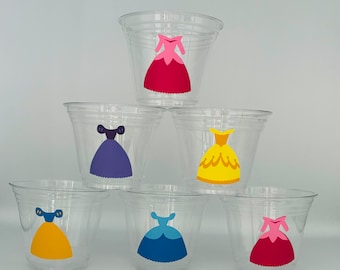May include: Six clear plastic cups with princess dress designs. The dresses are in various colors, including pink, purple, yellow, blue, and red.
