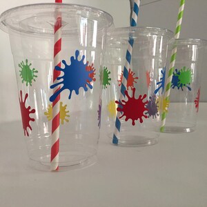 May include: Three clear plastic cups with colorful paint splatter designs and red and white striped straws.