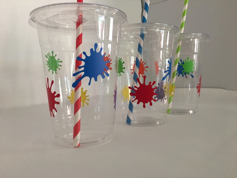 May include: Three clear plastic cups with colorful paint splatter designs and red and white striped straws.
